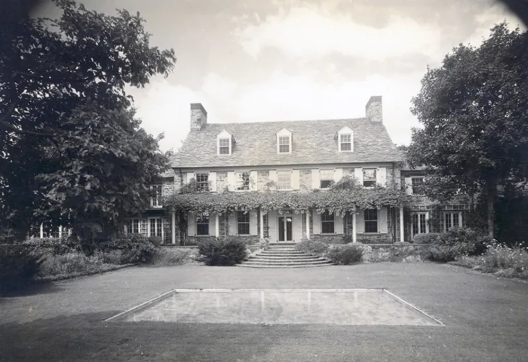 A historic estate with ivy-covered facade, multiple chimneys, and a large central lawn with a rectangular reflecting pool in the foreground.