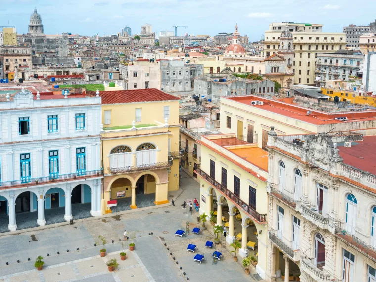Aerial view of a bustling cityscape with colorful historic buildings, arched windows, and a spacious plaza below.