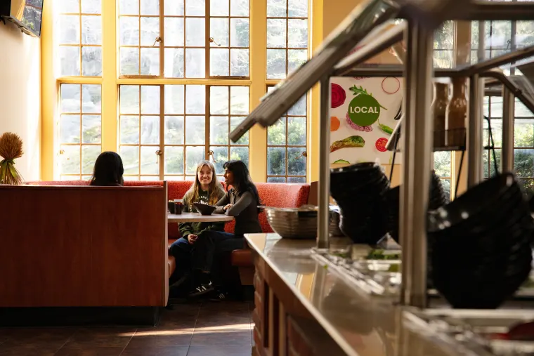 Two people sitting at a red booth in a brightly lit cafe, talking and smiling, with a salad bar in the foreground.