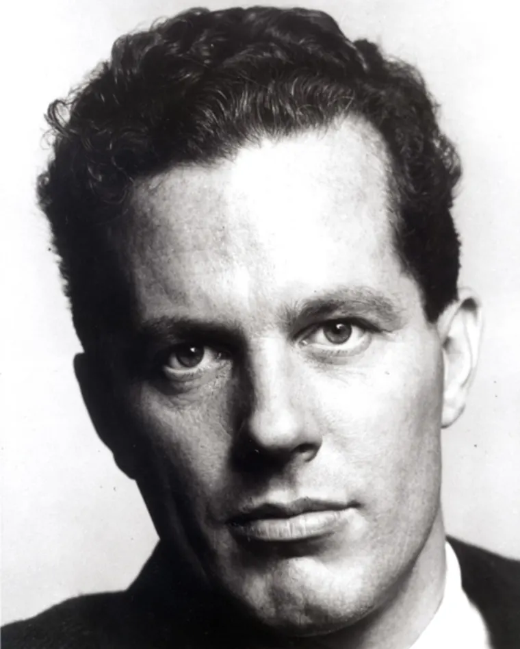 Black and white close-up portrait of a person with short curly hair, looking directly at the camera with a neutral expression.