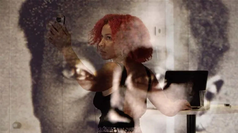 Person with red hair taking a selfie, standing in front of a black-and-white face projection.