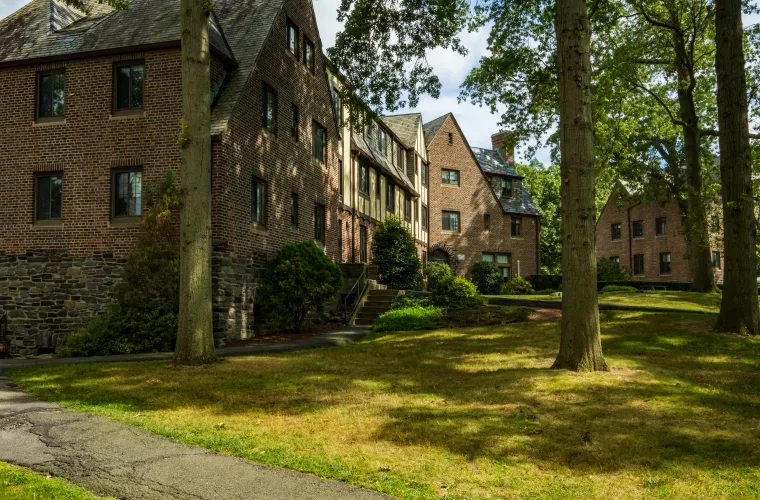 Brick buildings surrounded by trees and a grassy lawn, with a paved walkway curving through the foreground.