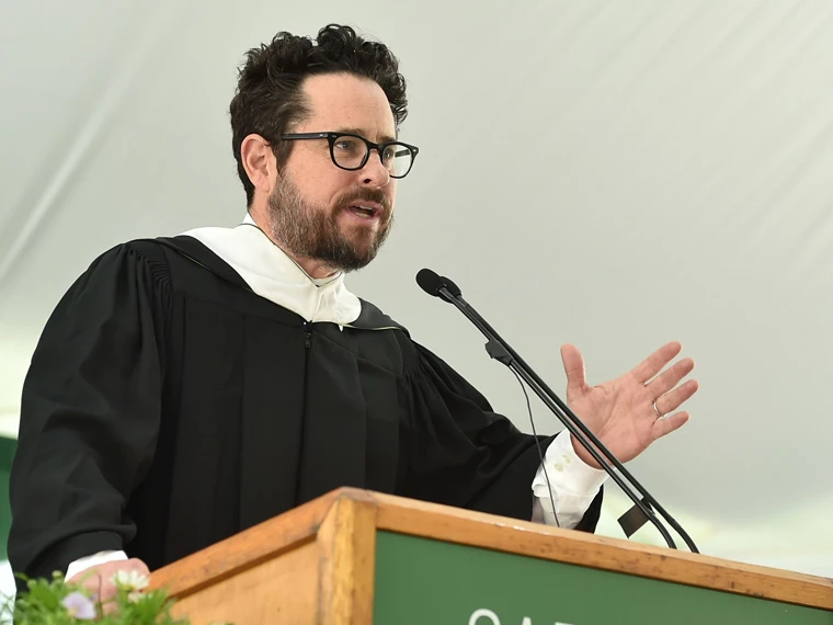 Person in academic robe speaks at a podium with a microphone, gesturing with one hand.
