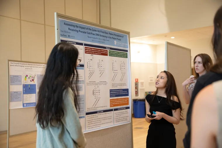 People discussing a research poster on patient perceptions and DNA screening at an academic conference.