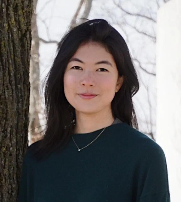 Person with dark hair wearing a teal top stands by a tree, with snow-covered branches in the background.