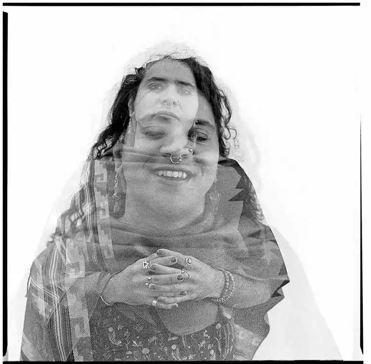 A double exposure photo shows overlapping images of a smiling face and clasped hands adorned with rings against a white background.