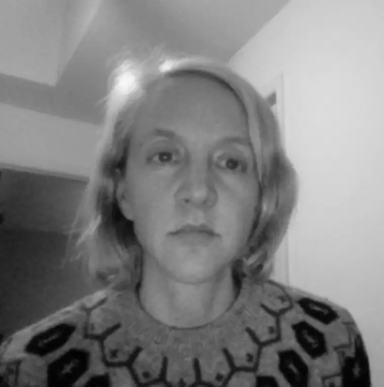 A person with medium-length hair wearing a patterned sweater looks at the camera in a black and white photo.