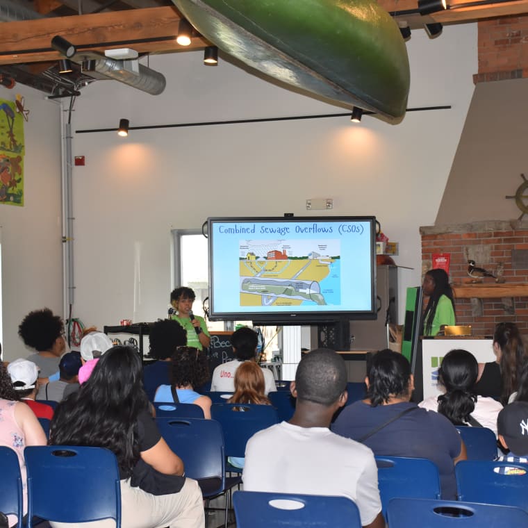 Person presenting on combined sewage overflows to an audience in a classroom with a large display screen showing a diagram.