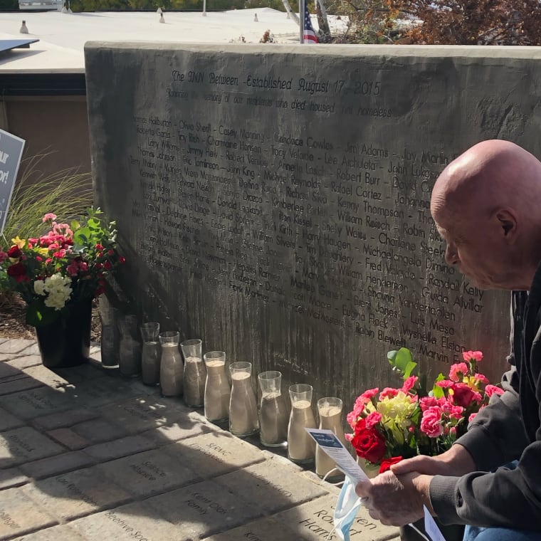 Resident kneeling near a stone memorial with names etched in the surface