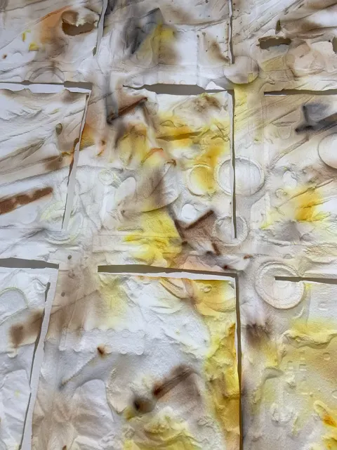 Abstract close-up of textured paper with overlapping layers, featuring smudges of brown and yellow, resembling watercolor and burnt marks.