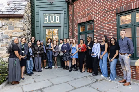 A group of people stands outside a building with a sign reading "Hub," posing for a photo while holding awards or plaques.