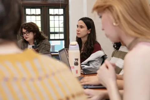 People sitting around a table with laptops, engaged in discussion. A water bottle with a bear sticker is visible in the foreground.