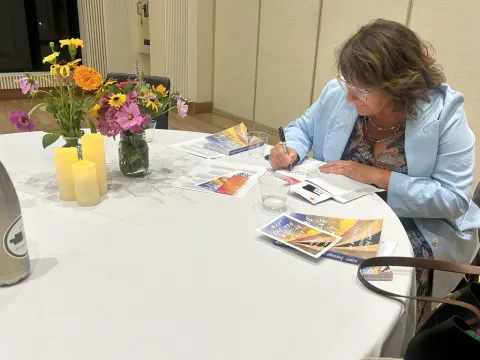 Person in blue attire writing at a round table with flowers, candles, and brochures.