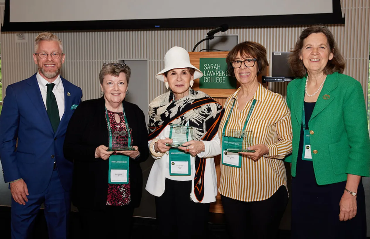 Five individuals stand together smiling, four holding awards, in front of a podium with a Sarah Lawrence College sign.
