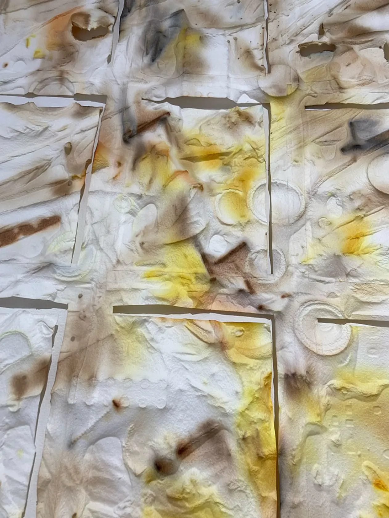 Abstract close-up of textured paper with overlapping layers, featuring smudges of brown and yellow, resembling watercolor and burnt marks.