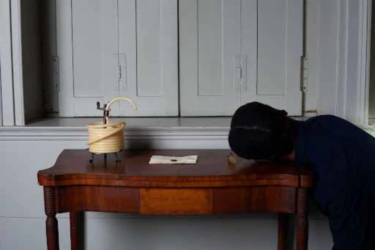 Person with head on a wooden table, next to a spool and envelope, in front of closed shutters.