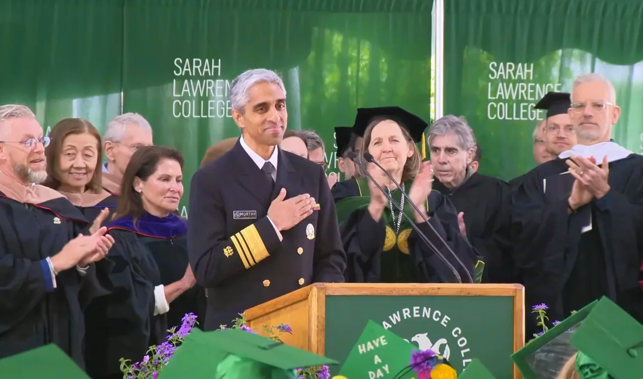 Person in military uniform stands at a podium during a graduation event at Sarah Lawrence College, surrounded by applauding individuals in academic regalia.