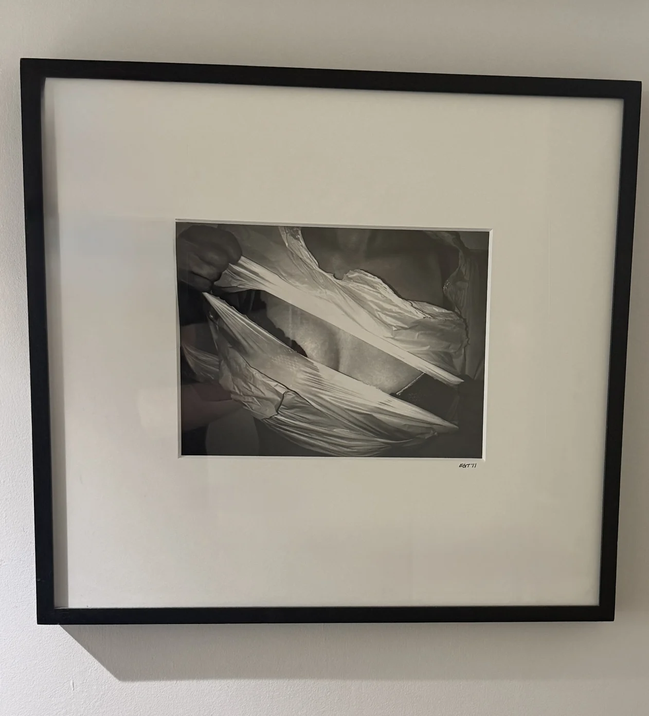 Framed black-and-white photograph of fabric being pulled apart, forming dynamic creases and shadows.