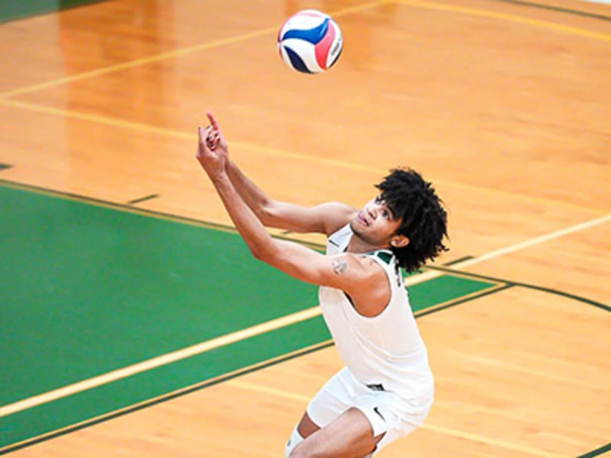 Volleyball player jumping to hit the ball on an indoor court, wearing a white jersey and shorts.