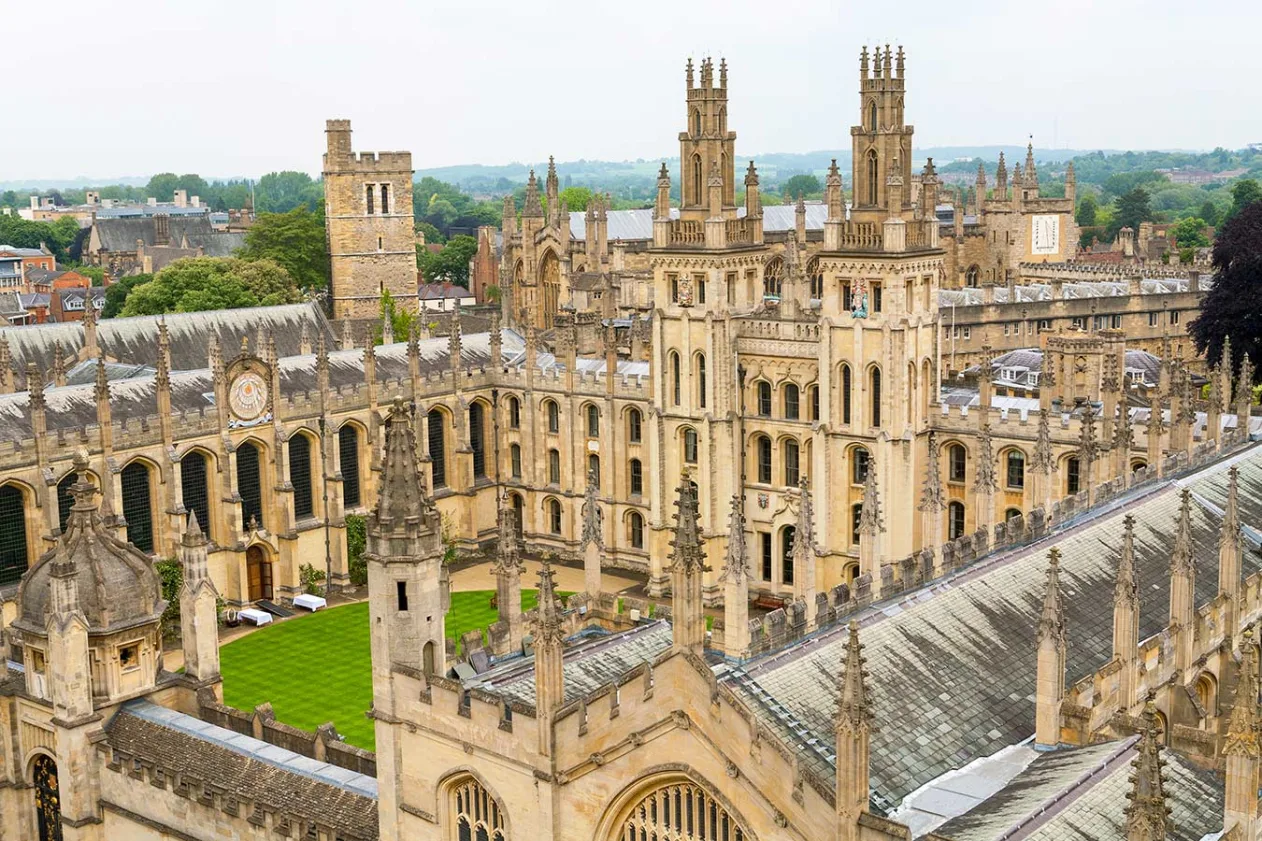 Aerial view of a historic university building complex with intricate architecture, spires, and a green courtyard.