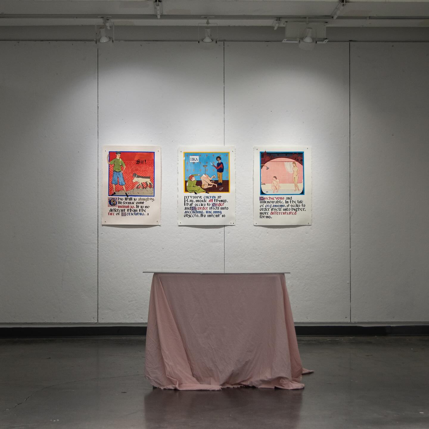 Three framed posters on a wall above a draped table in an exhibition space.