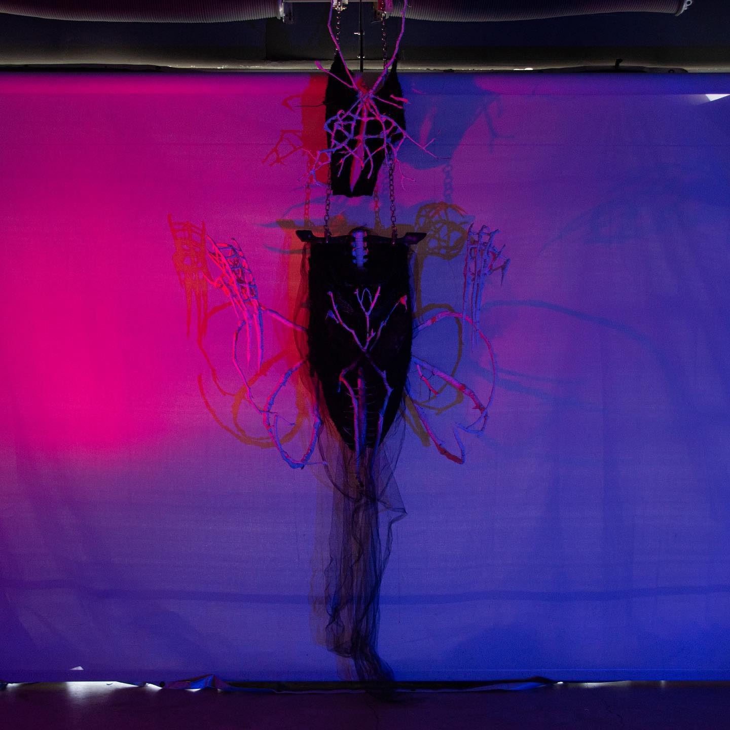 Artistic installation with black form and chains against a purple background.