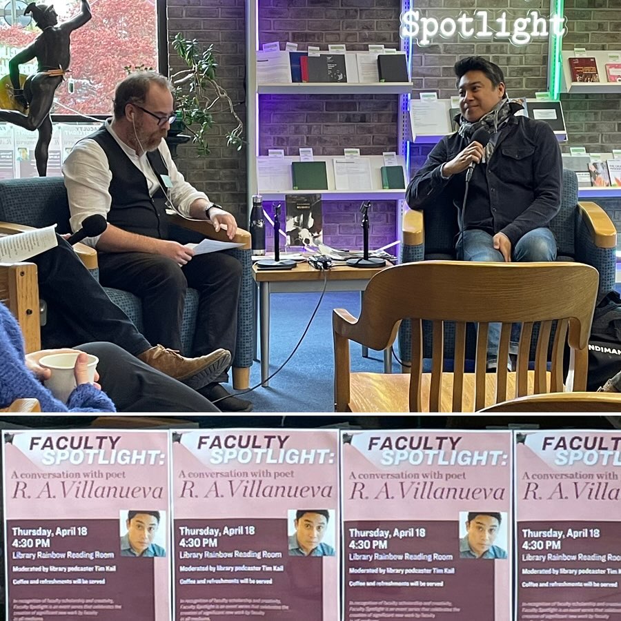 Two individuals seated with microphones at a public speaking event with event posters in the foreground.