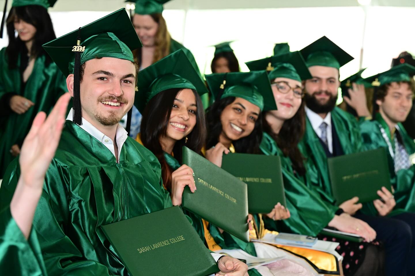 Graduates in green caps and gowns holding diplomas, smiling at a ceremony.