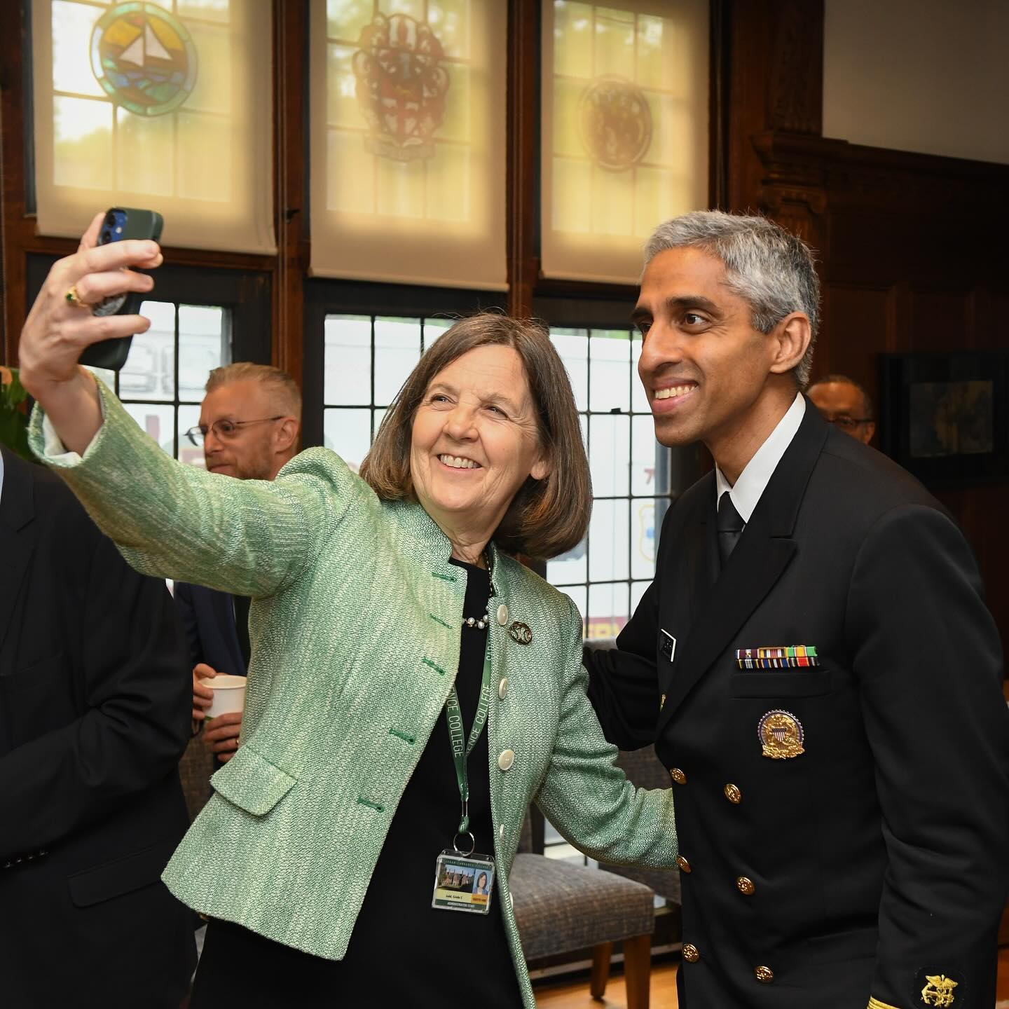 Two smiling individuals taking a selfie, one in a green jacket, the other in a navy uniform.