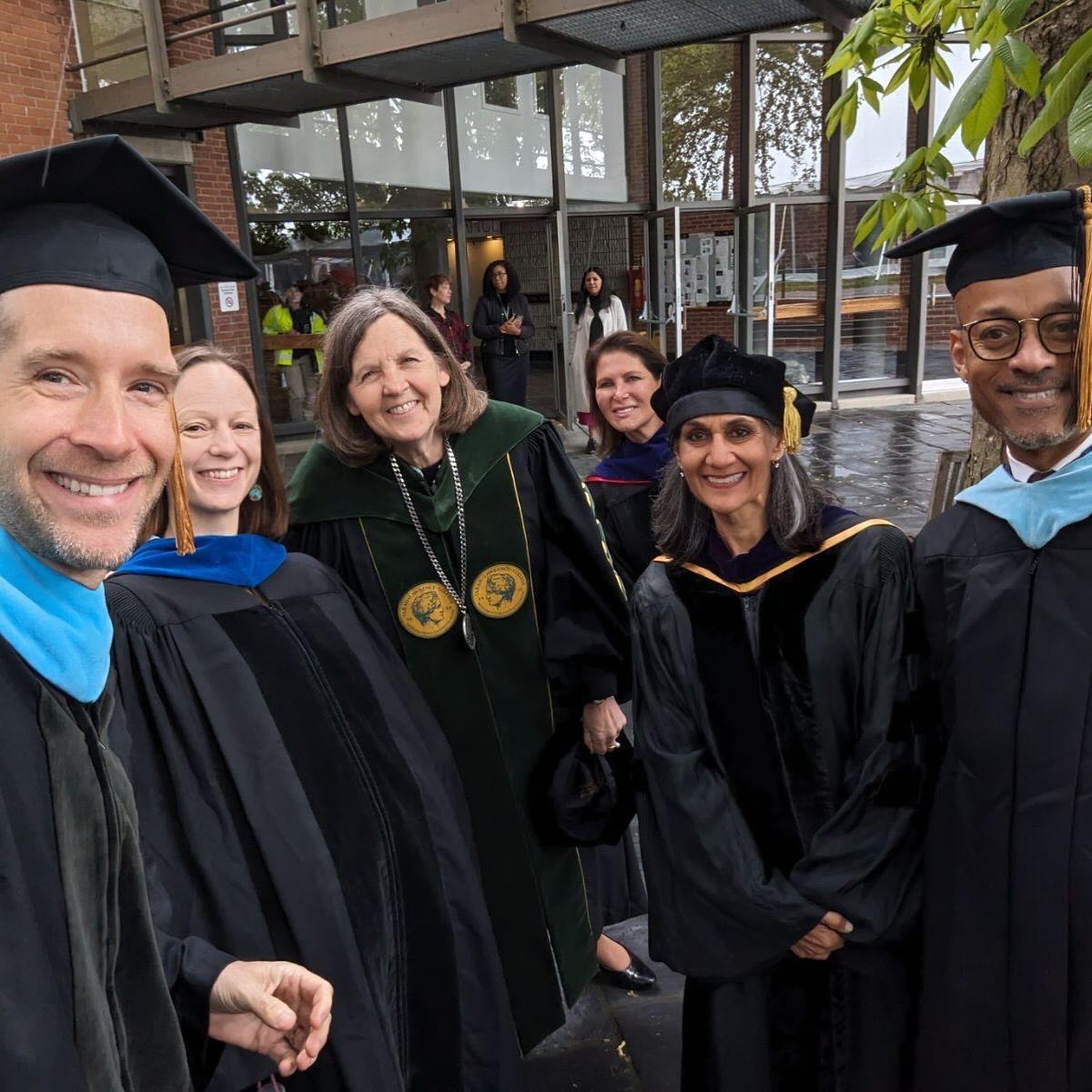 Group of individuals in academic regalia smiling outside a building.