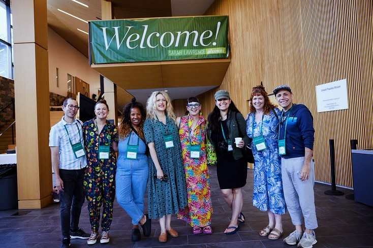 Group of people smiling under a 'Welcome!' banner at Sarah Lawrence alumni event.