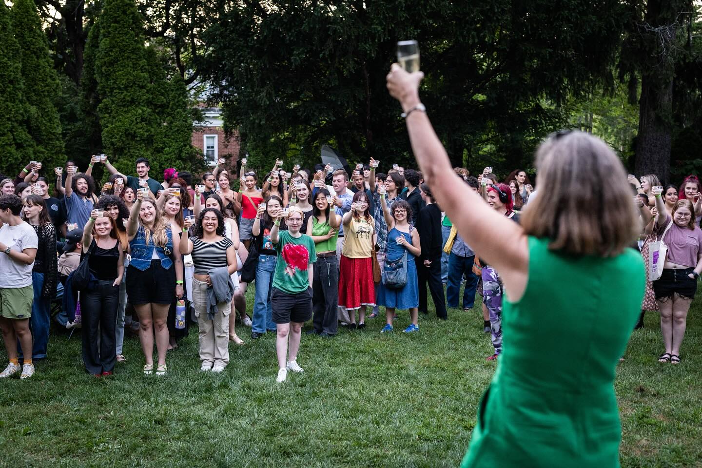 A person in a green dress taking a selfie with a cheering crowd in the background.