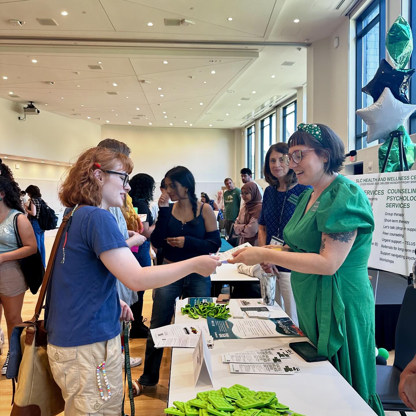 Individuals exchanging paperwork at a busy informational event with a crowd in the background.