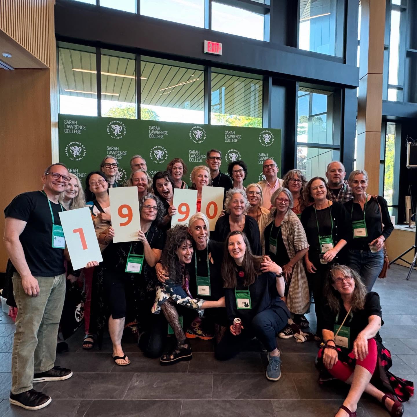Group photo of people at a Sarah Lawrence College event indoors, holding signs showing the year &quot;1990.&quot;