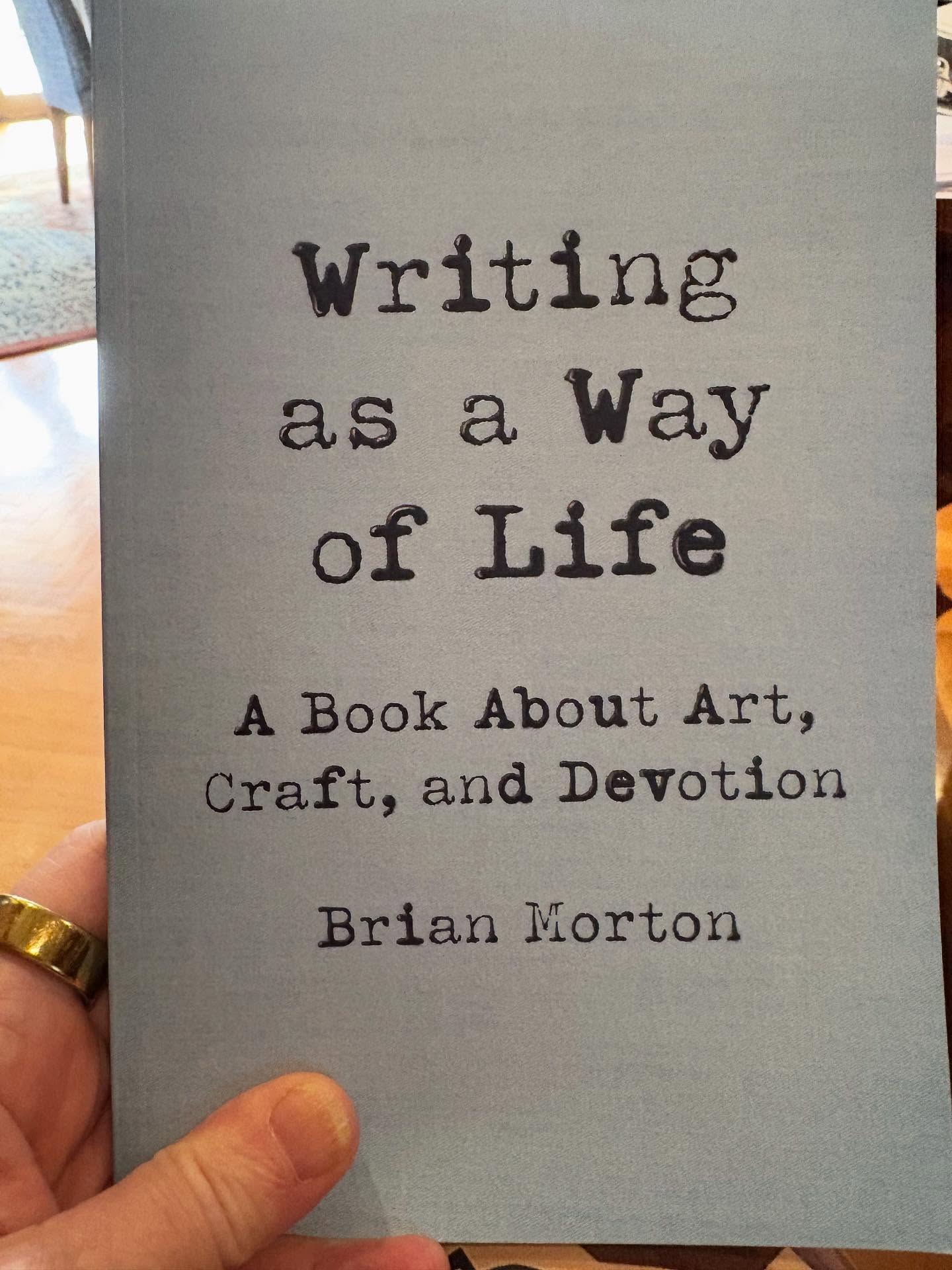 A hand holds a book titled "Writing as a Way of Life: A Book About Art, Craft, and Devotion" by Brian Morton.