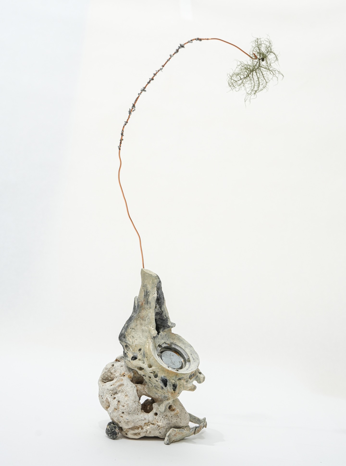 Abstract sculpture with a textured, stone-like base and a long, thin wire extending upwards, ending in wispy, net-like material.