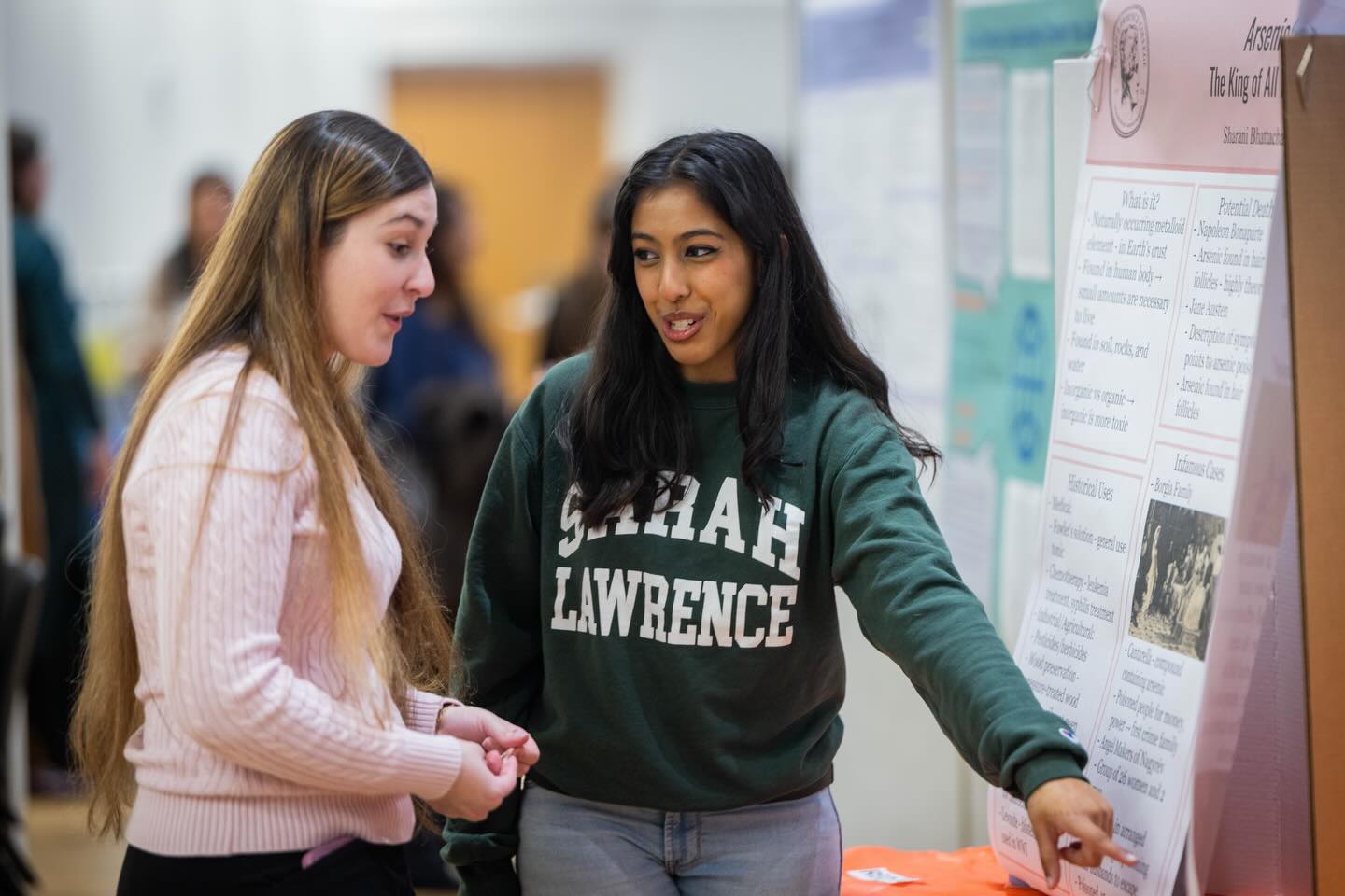 Two people stand near a presentation poster. One points to the poster while the other listens attentively.