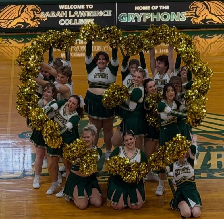 Cheerleaders in green and gold uniforms form a heart shape with gold pom-poms on a gym floor. "Welcome to Sarah Lawrence College" sign above.