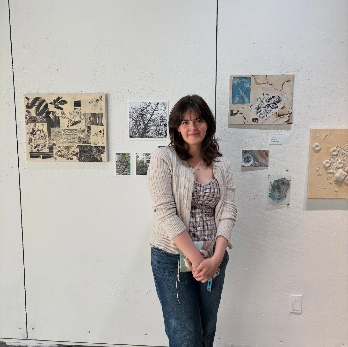 Person standing in front of a gallery wall displaying various artworks, including collages and abstract pieces.