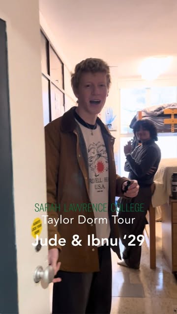 Two people in a dorm room, one by the door smiling, the other standing by bunk beds. Text overlay reads: "Sarah Lawrence College Taylor Dorm Tour Jude &amp; Ibnu ’29".