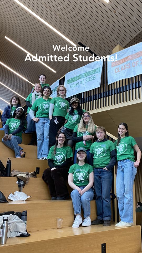 Group of people in matching green shirts with "Sarah Lawrence College" design, posing on stairs under banners for Class of 2028 and 2029.