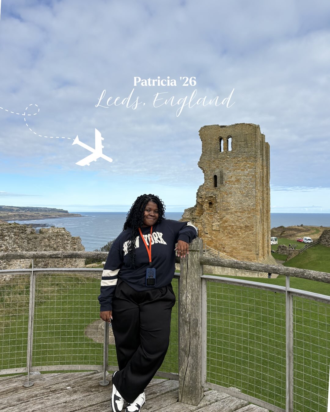 Person in a New York sweater stands on a wooden platform by a stone tower, with a grassy area and sea in the background. Airplane graphic in sky.