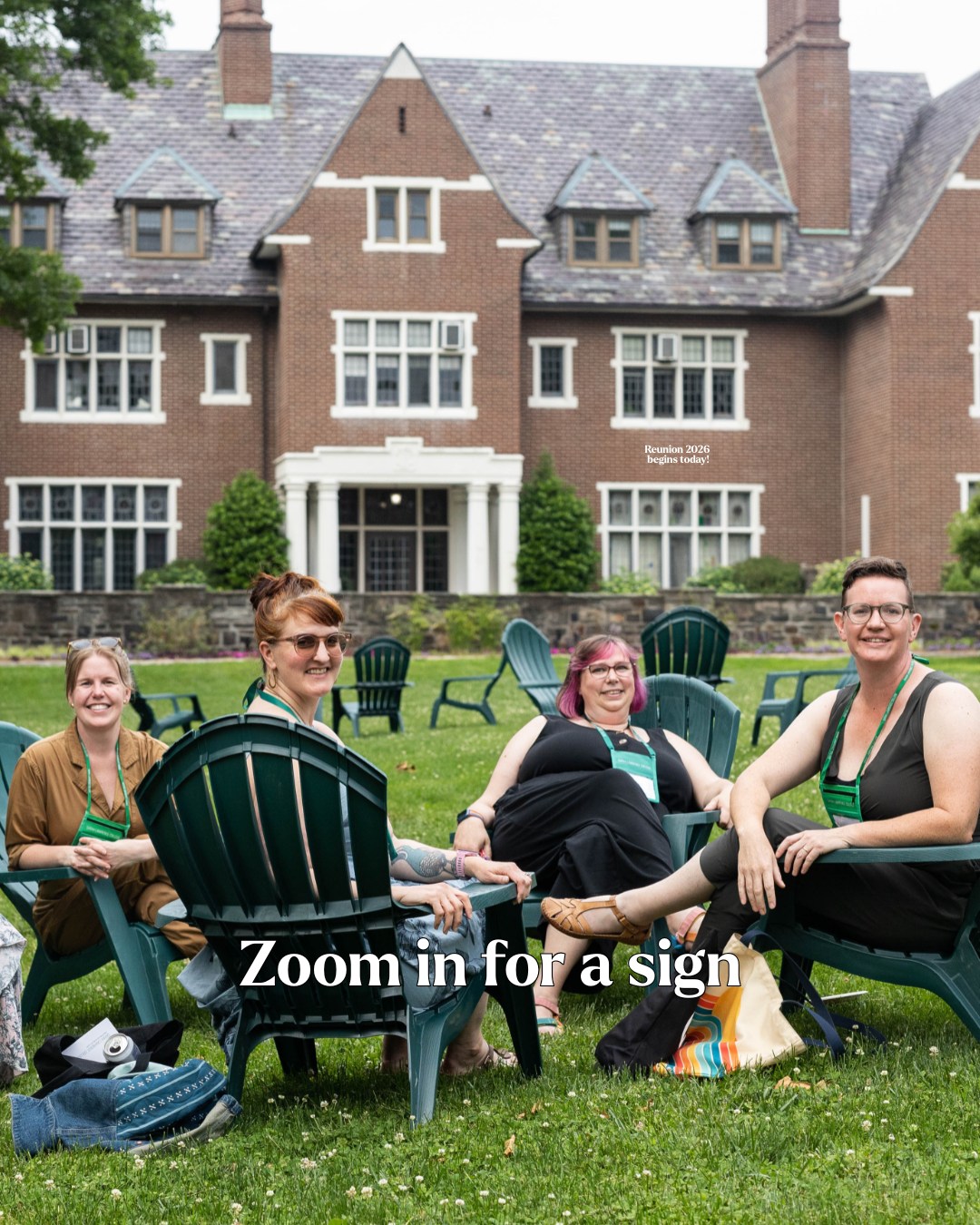 Four people sitting in outdoor chairs on a lawn in front of a large brick building. Text on image reads "Zoom in for a sign."