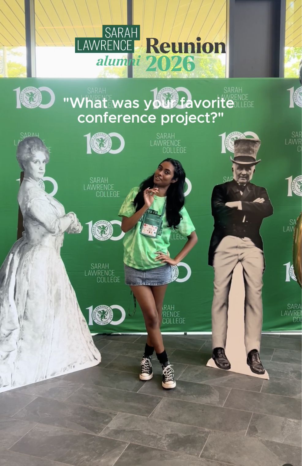 Person in a green shirt posing between two historical figure cutouts at a Sarah Lawrence College reunion backdrop.