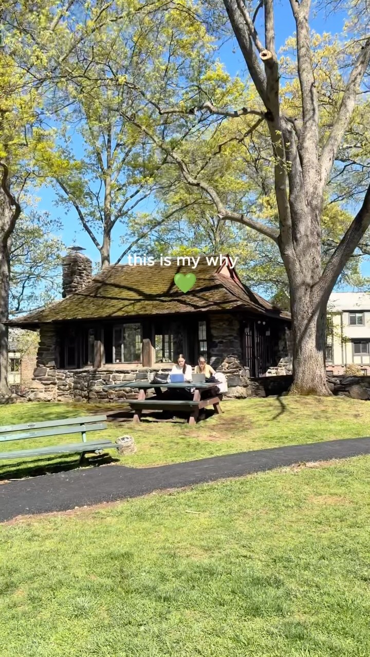 Stone cottage surrounded by trees; two people sit at a picnic table with laptops. Text reads: "this is my why" with a green heart emoji.