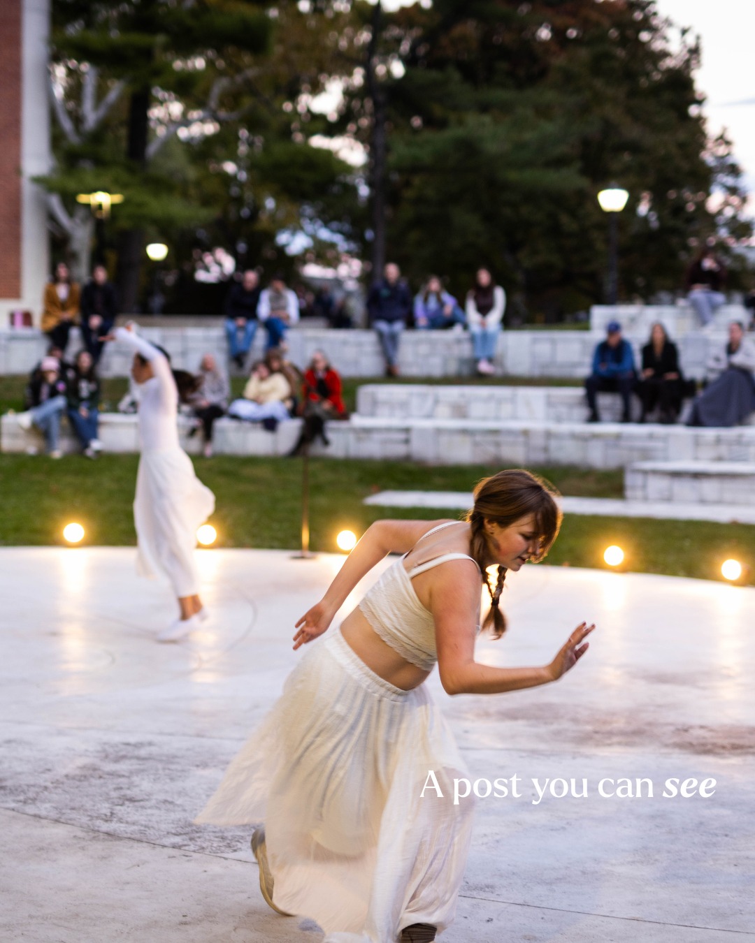 Person in flowing white outfit dances outdoors, with spectators seated on stone steps in the background. Text reads “A post you can see.”