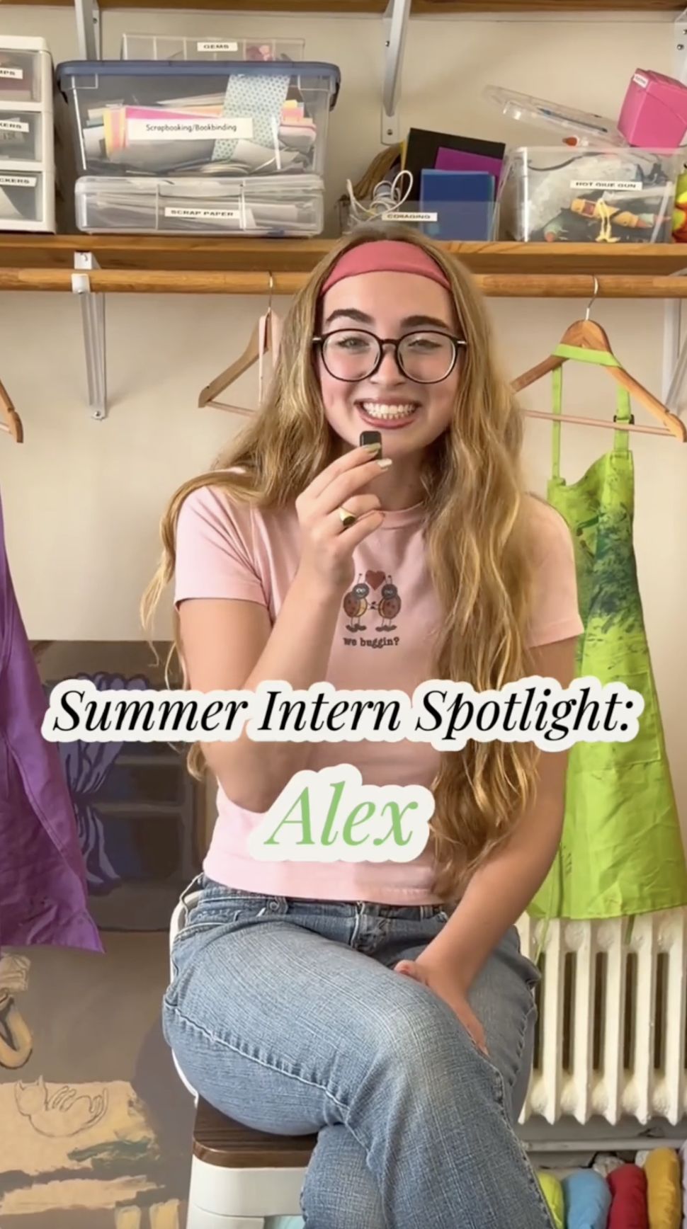 Person with long hair and glasses sits smiling, holding a microphone. Text reads "Summer Intern Spotlight: Alex." Colorful fabrics around.