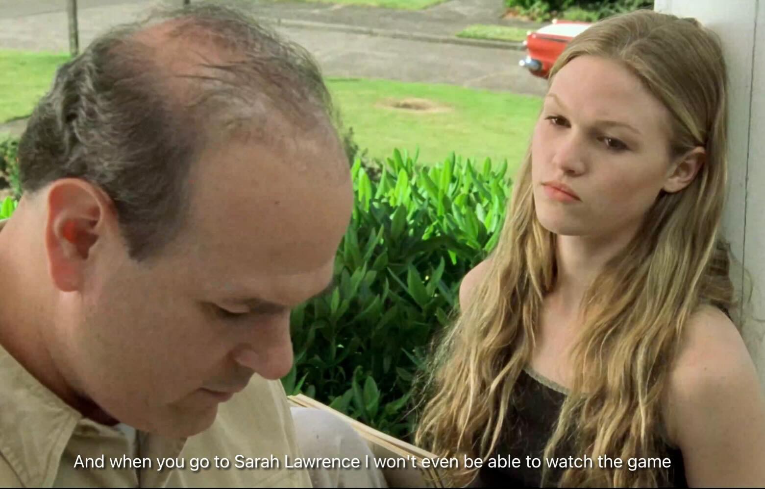 Two people are on a porch. One is looking down, holding papers. The other leans on the wall, appearing contemplative. Subtitles mention "Sarah Lawrence."
