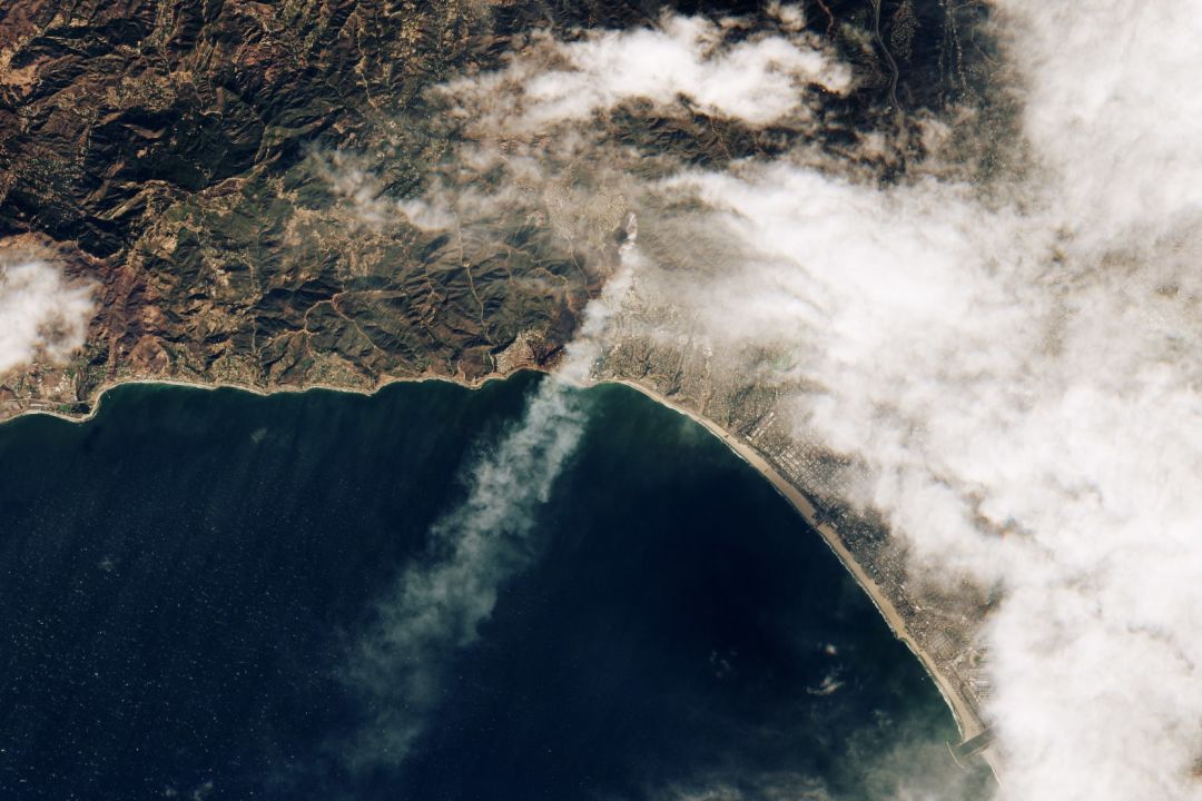 A satellite image of the Palisades Fire, with smoke streaming over the Pacific Ocean.