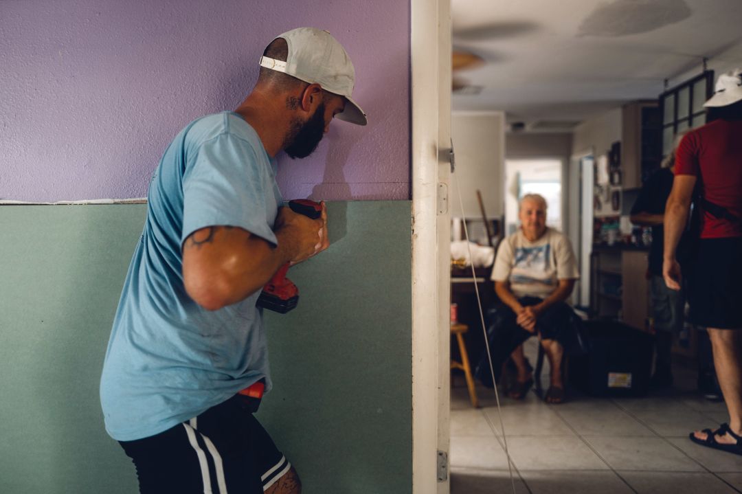In Cortez, Austin Simmoneau works on repairs as homeowner Sally McAllister rests in the living room.